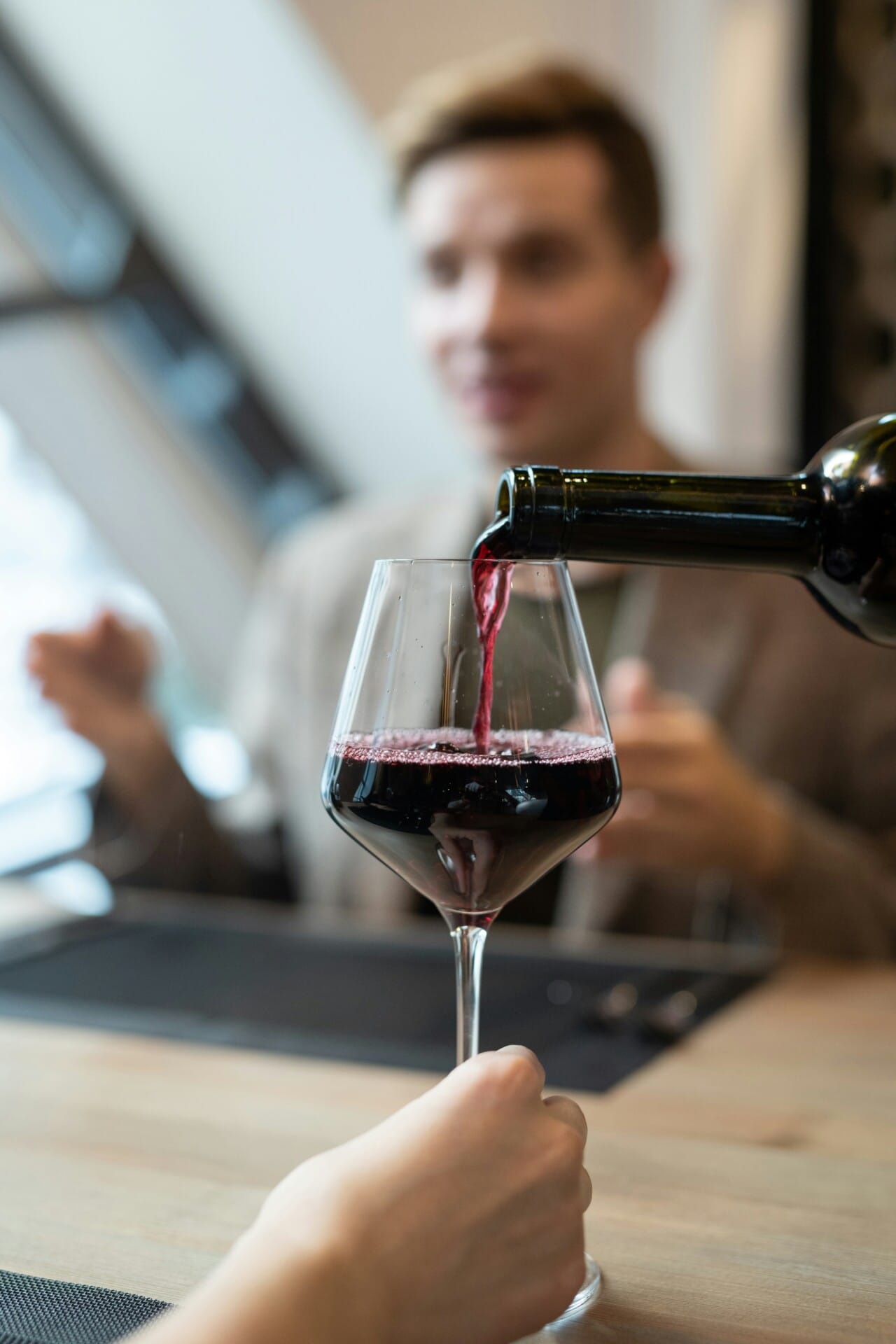 Rotwein wird in Glas eingeschenkt, unscharfer Hintergrund.