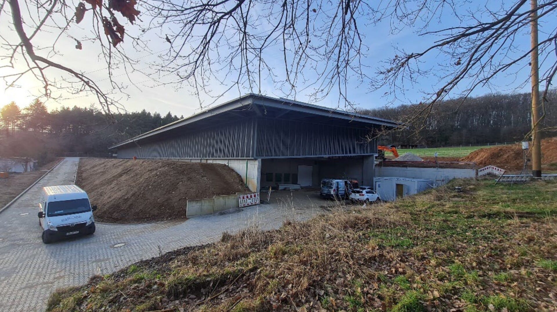 Lagerhalle mit Fahrzeugen und Bäumen im Hintergrund.